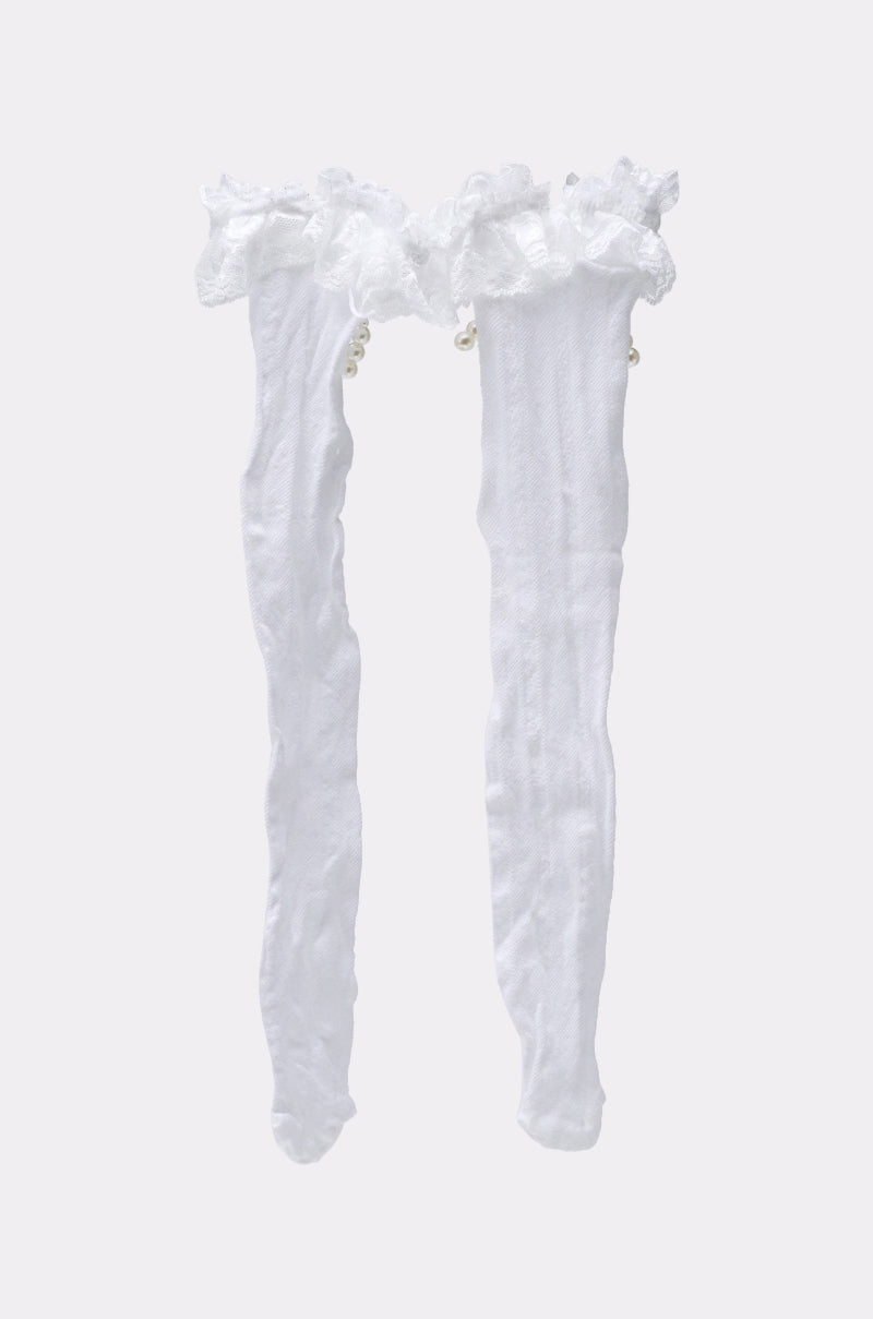 RUFFLE MANIA KNEE HIGH SOCKS: White knee-high socks with a ruffle trim and sheer texture, shown on a light gray background. Decorative details near the top combine elegance with playful style.
