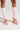 A person is standing and wearing the "WITH THE TREND LEG WARMERS," which feature a white and light pink knit fabrication, paired with high-heeled platform shoes adorned with a floral pattern. The background is a plain white surface.