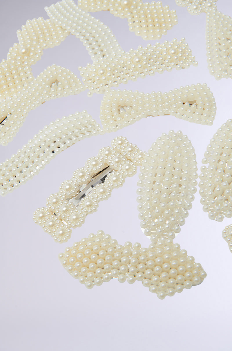 A set of ROCKI HAIR CLIP SET from the AKIRA Label displayed on a light background, showcasing various shapes like rectangles and bows, all elegantly adorned with pearl embellishments. 4