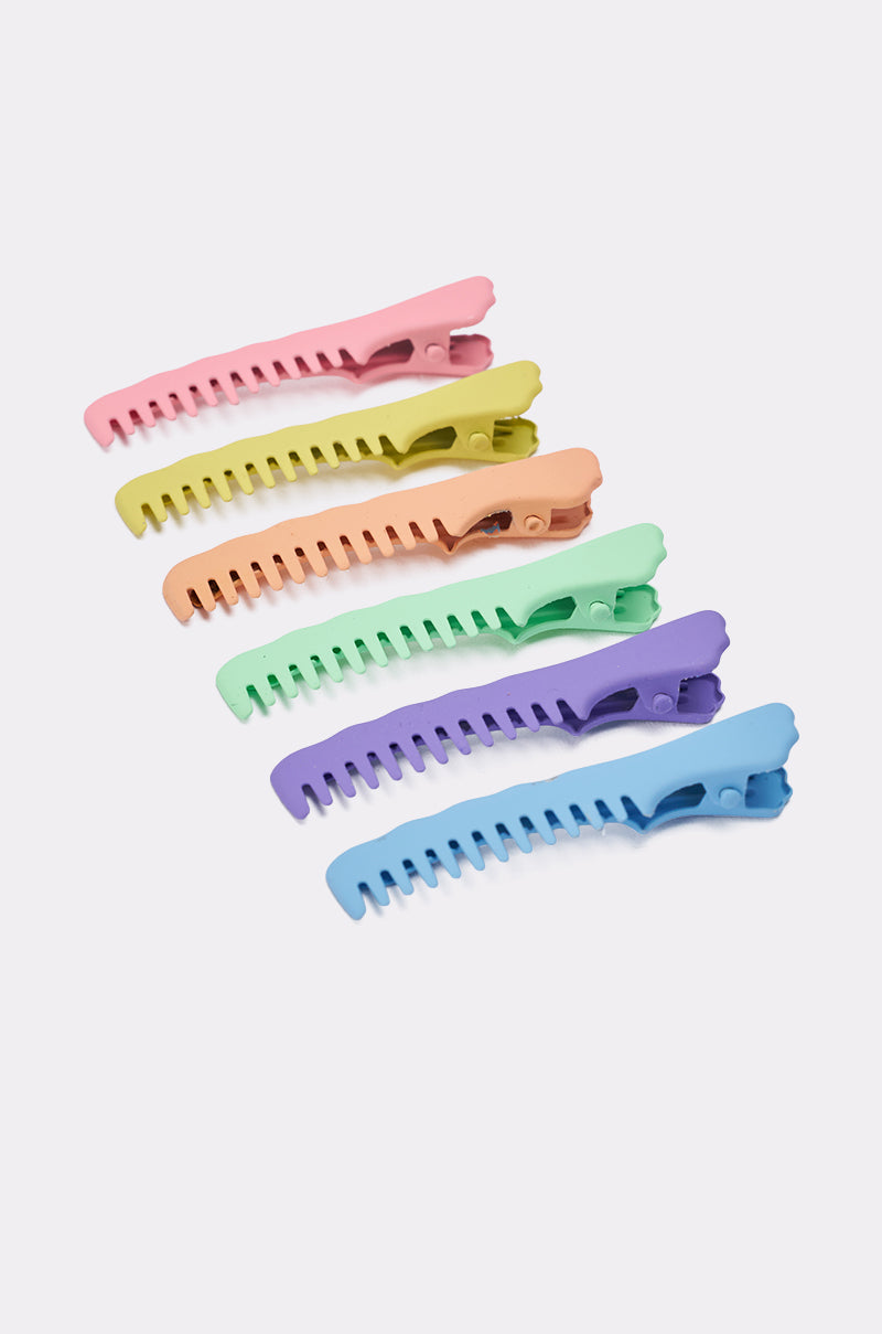 Five pastel COMB HERE HAIR CLIP SET barrettes, each with a stylish ridged design in pink, yellow, orange, green, and blue, are arranged diagonally on a white background. 1