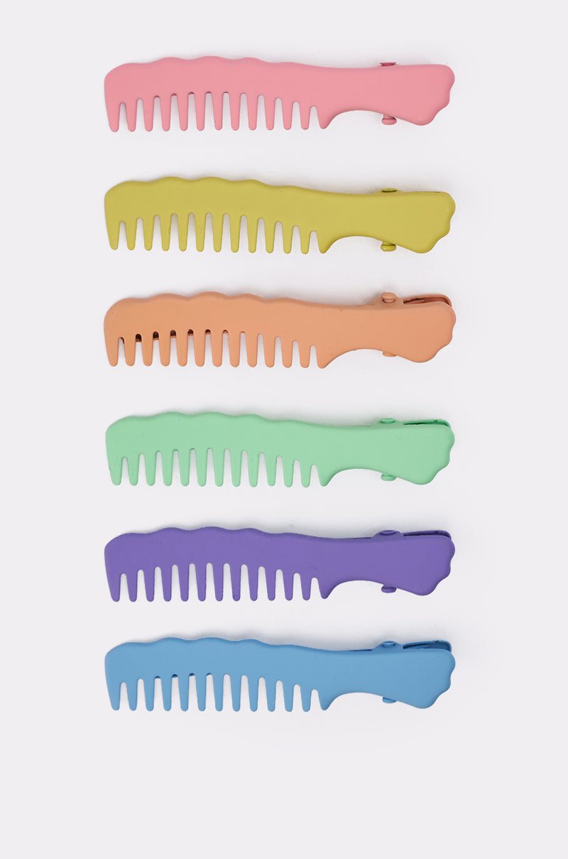 The COMB HERE HAIR CLIP SET features six brightly colored comb-shaped barrettes—pink, yellow, orange, green, purple, and blue—arranged vertically on a white background for a fun pastel hair accessory look. 2