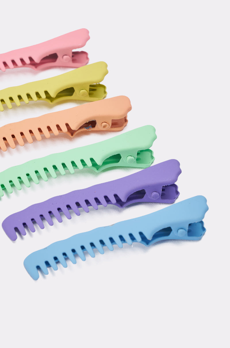 The COMB HERE HAIR CLIP SET includes six pastel comb-shaped barrettes in pink, yellow, orange, green, purple, and blue, shown diagonally on a white background. 4