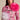 A person in a floral-patterned pink jacket with oversized white and pink TIS THE SEASON BROOCH SET exudes avant-garde romance. Their long dark hair cascades against a neutral backdrop, enhancing the organza-like elegance.