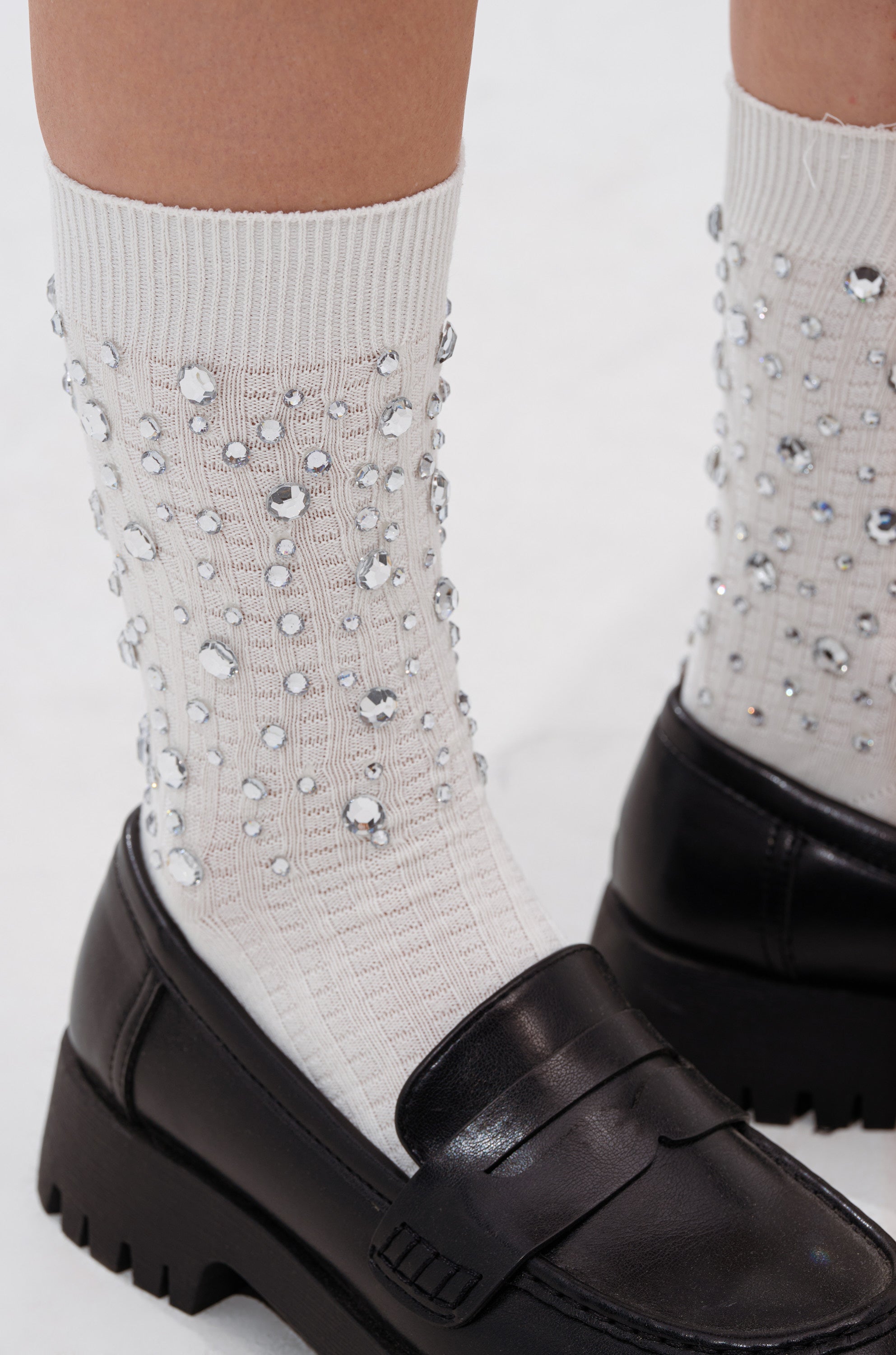 A close-up of feet in BLING BLING SOCKS—white ribbed socks adorned with rhinestones—paired with chunky black loafers on a white surface.