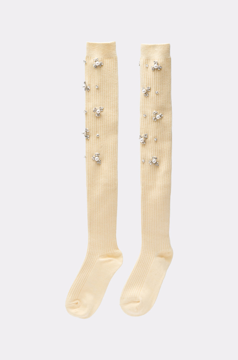 The COCO EMBELLISHED SOCKS IN CREAM are knee-high, cream-colored socks featuring clusters of rhinestones and faux pearls in floral designs, adding a touch of elegance to any outfit. 1