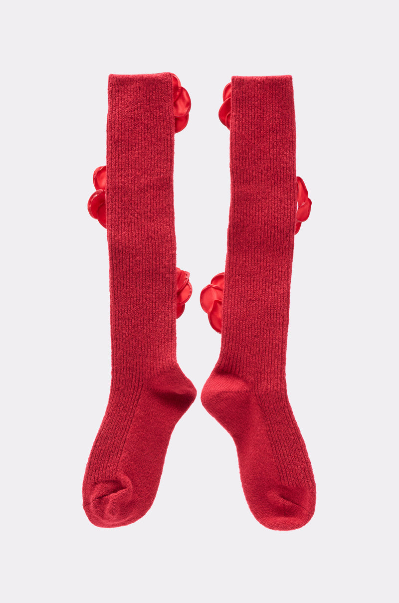 ROSIE SOCKS: Red knee-high socks with a ribbed texture and 3D rosette appliques on the sides, shown on a plain light gray background. 2