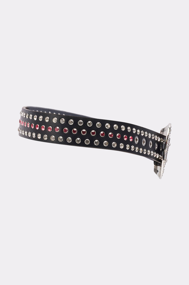 The "I AM THAT BELT" is a black faux leather belt with two rows of round silver and red studs and a large western buckle, shown against a plain white background. 6