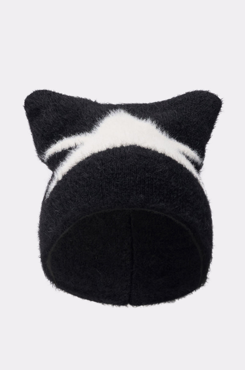 The IT GURL BEANIE is a black fuzzy knit hat with two pointed cat ears and a bold white zigzag stripe across the front, shown against a plain light background. 0