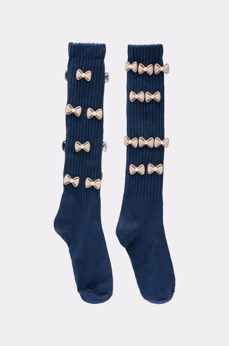 The BOW PLEASE CHARM SOCKS are navy blue, knee-high, and ribbed, featuring five sparkly light bows arranged vertically on the outer side for a charming embellished look. 4