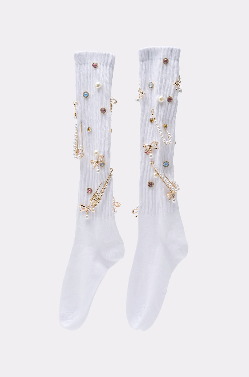 ON TREND CHARM SOCKS: Long white socks adorned with jeweled embellishments, pearls, and gold-toned accents in stylish patterns—perfect for fashion-forward accessory lovers. 1