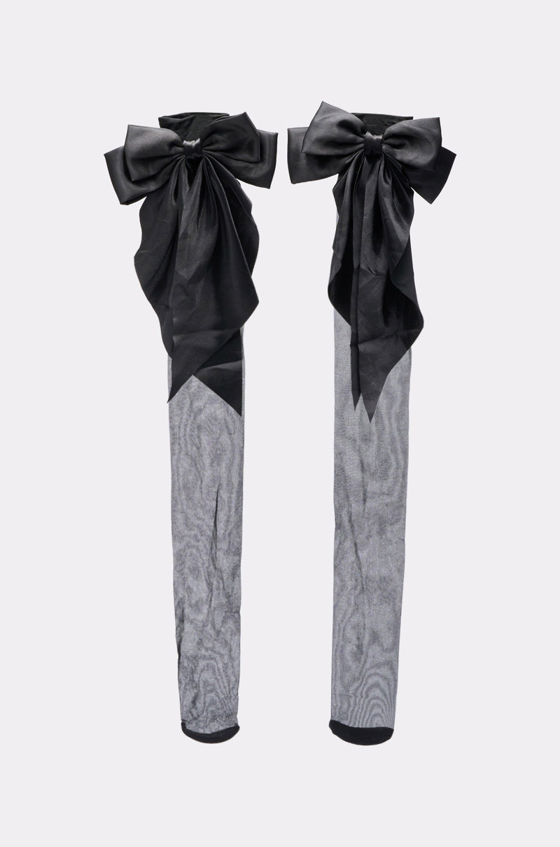 The DRESS ME UP BOW STOCKINGS are sheer gray stockings with large decorative black satin bows at the top, shown against a plain light background. 2