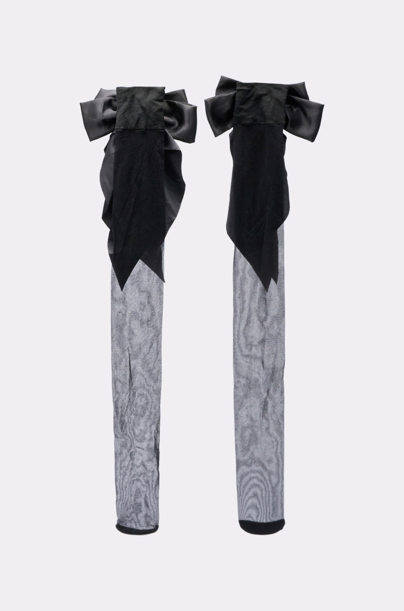 The DRESS ME UP BOW STOCKINGS are sheer, knee-high grey socks featuring black satin bows and decorative black fabric accents at the top, displayed upright against a plain white background. 3