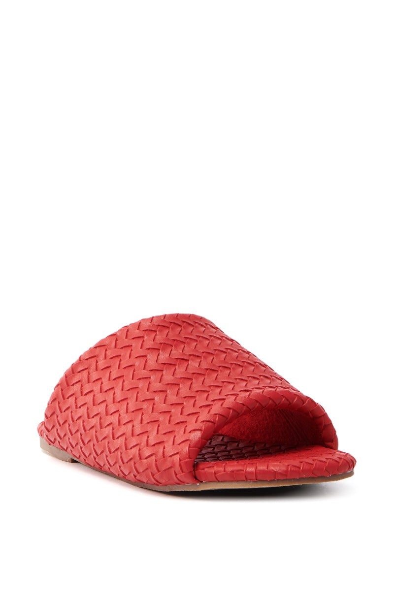The AKIRA GAIA RED BRAIDED FLAT SLIP ON SANDAL, featuring a cherry red braided open toe with an elegant faux leather design and flat sole, is displayed against a white background.