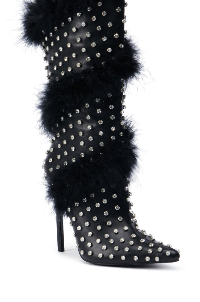 The AZALEA WANG GARDENIA FEATHER EMBELLISHED BOOT IN BLACK is a sophisticated high-heeled black faux leather boot accented with silver studs and black fur trim. Its pointed-toe design and tall stiletto heel offer a blend of fashion and bold style, with discreet feather embellishments adding a whimsical touch.