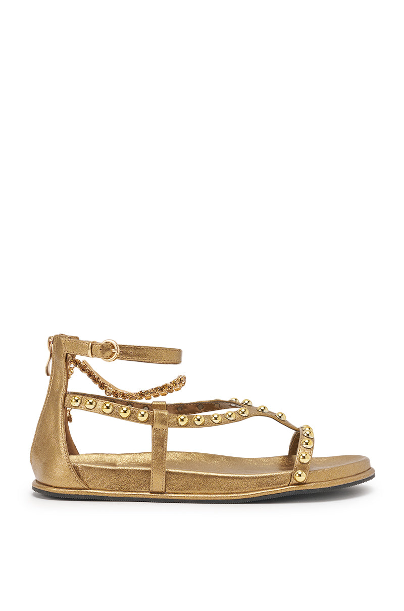 The AKIRA GATO BRONZE GOLD METAL EMBELLISHED FLAT SANDAL features ankle and foot straps with gold studs, a slim ankle buckle, and a back zipper in metallic faux leather, shown in side view on a white background. 3