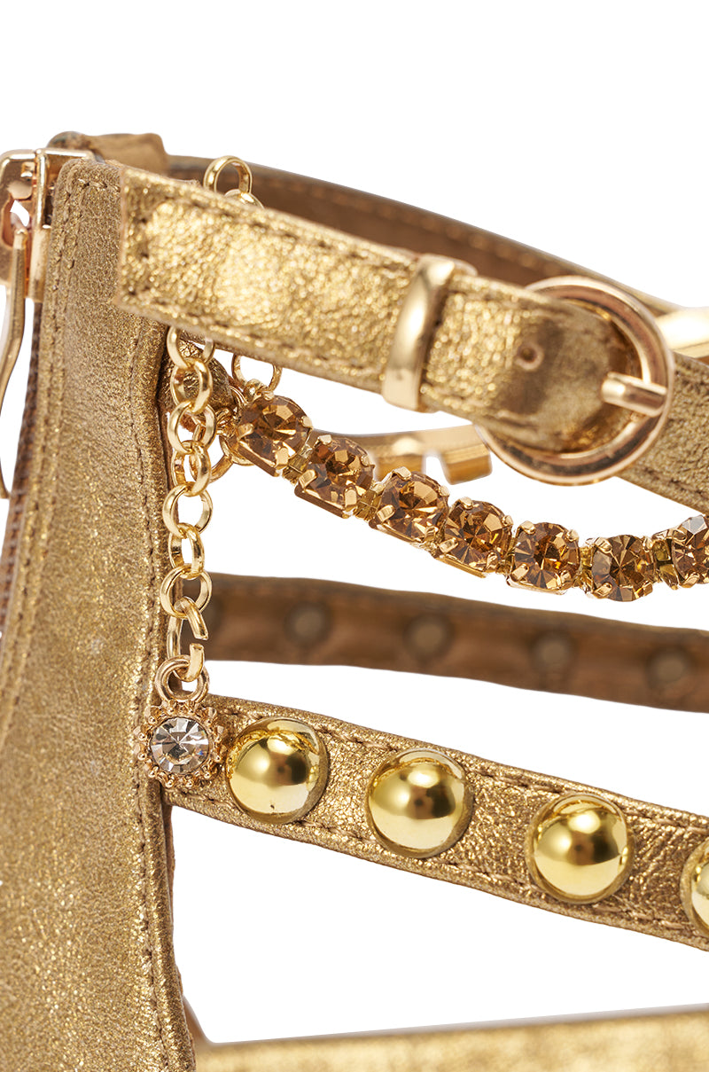 Close-up of the AKIRA GATO BRONZE GOLD METAL EMBELLISHED FLAT SANDAL, showcasing its gold textured faux leather, metallic studs, rhinestone chain accents, and buckle strap for a stylish and eye-catching flat sandal design. 6