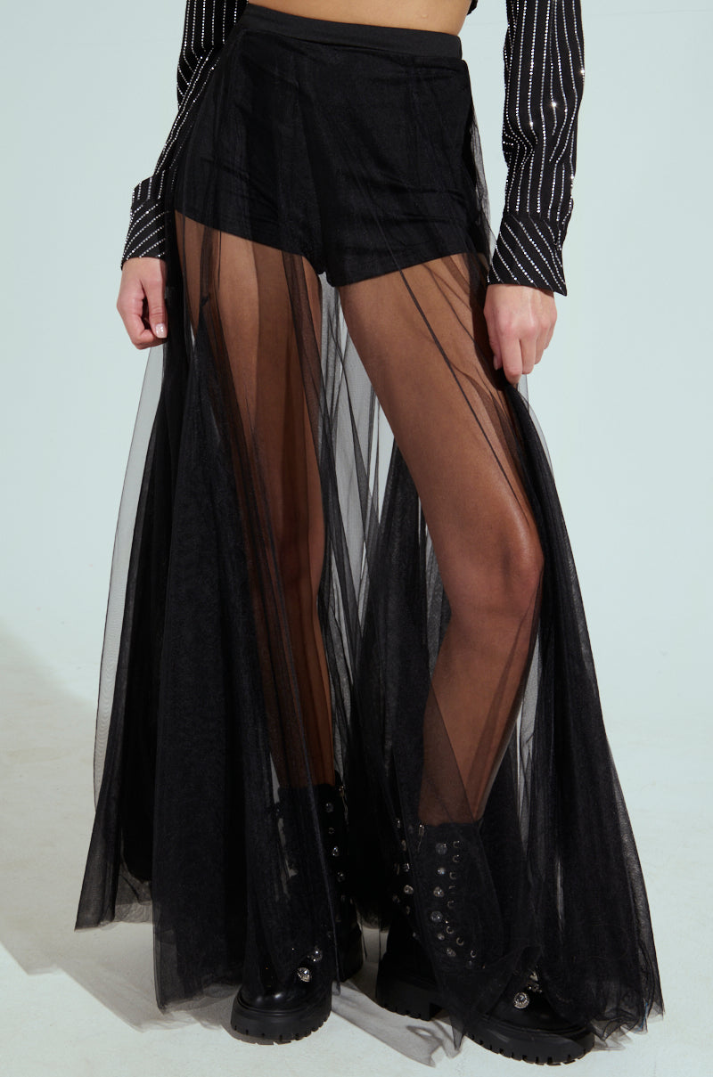 A model showcases the MY ALL MAXI TULLE SKIRT, layered sheerly over high-rise black shorts. The ensemble features a striped long-sleeve top and black combat boots, all set against a plain light background.