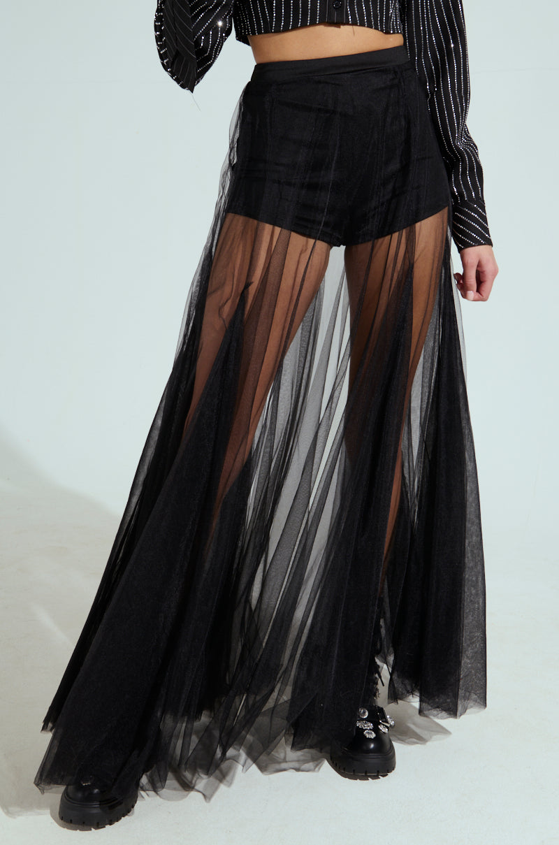 A person wearing a black pinstripe blouse is shown from the waist down, sporting the MY ALL MAXI TULLE SKIRT—a pair of black shorts with a sheer pleated tulle skirt overlay—accompanied by chunky black boots against a plain white background.
