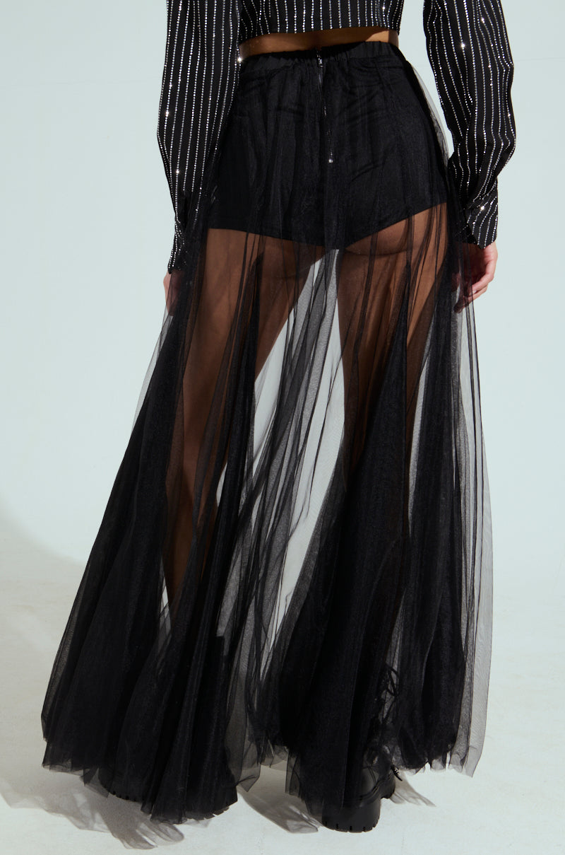Someone is seen wearing the MY ALL MAXI TULLE SKIRT in black, featuring an elastic waistband and black shorts underneath. It's paired with a black-and-silver striped long-sleeve top against a simple, light background that highlights the skirt's elegance.