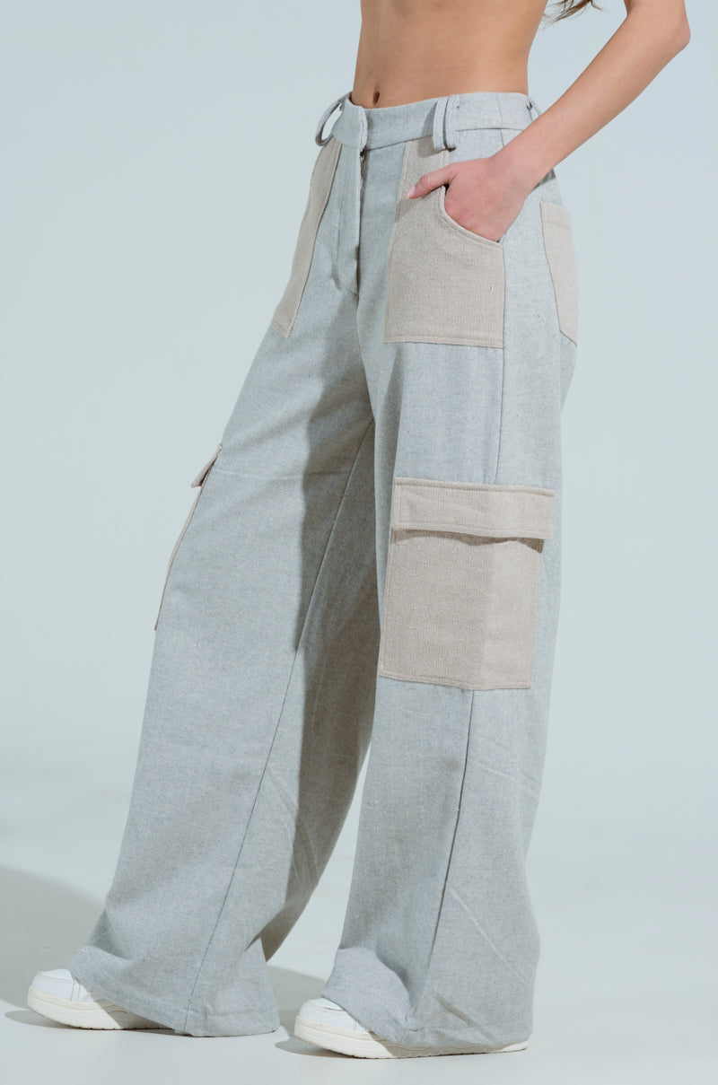 A person wears the light gray wide-leg TO LOVE AGAIN TROUSER with a high-rise waistband and large pockets, paired with white sneakers. Their midriff is bare, hand in one pocket, against a plain light-colored background for a casual look.