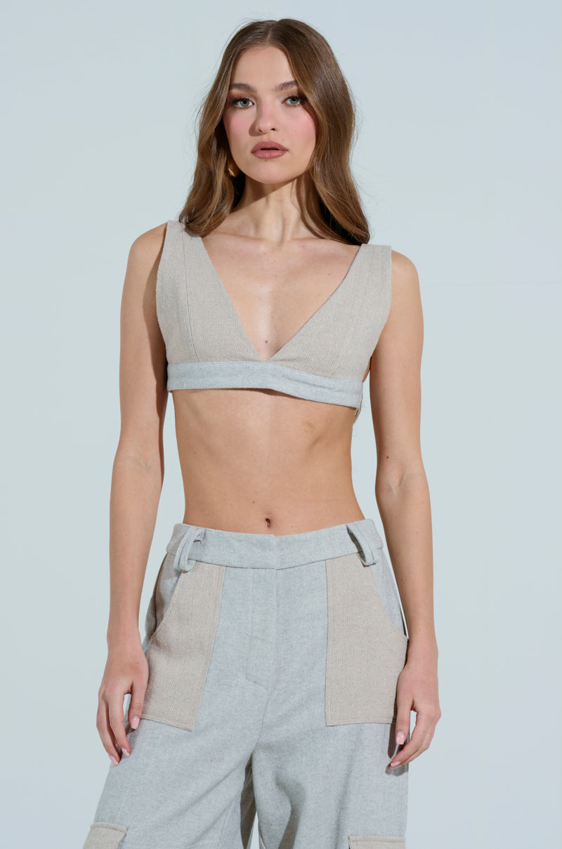 A woman with long hair wears a TO LOVE AGAIN BRALETTE in beige wool blend and gray high-waisted pants with structured lines and large pockets, standing against a plain background facing forward with a neutral expression.