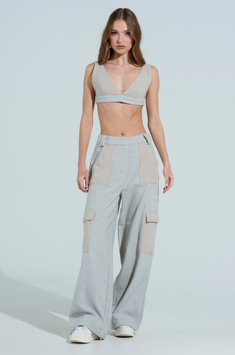 A woman stands wearing a gray, two-piece outfit featuring the TO LOVE AGAIN BRALETTE, a wool blend sleeveless crop top, and wide-legged pants with large pockets. She pairs it with white sneakers against a plain, light-colored background.