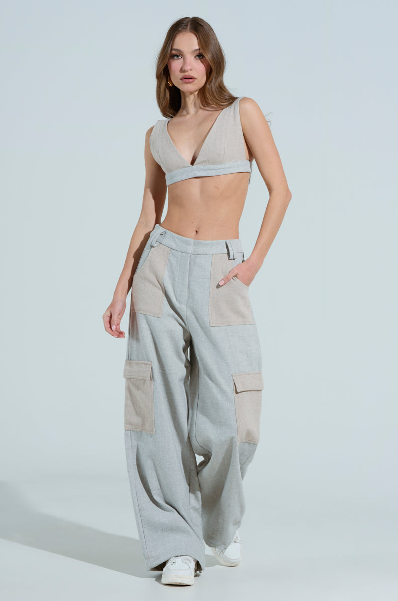 A person with long hair wears the TO LOVE AGAIN BRALETTE in beige wool blend and gray cargo pants, paired with white sneakers. They stand against a light background, one hand in a pocket while the other hangs by their side.