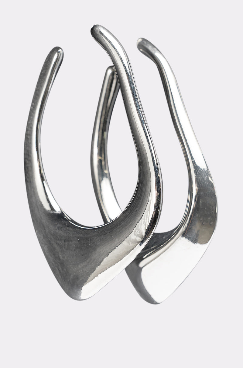 The DRIPPY EARRING is a pair of modern, silver-tone statement earrings featuring an abstract, curved, pointed design, shown against a plain light background. 2