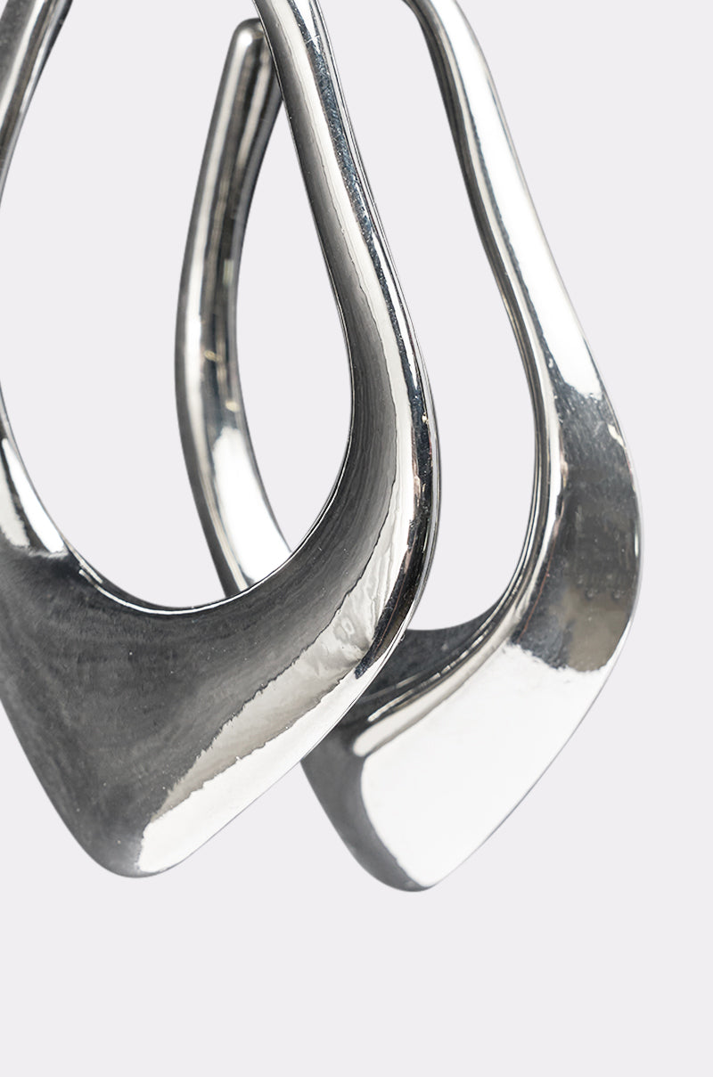 Close-up of the DRIPPY EARRING—two abstract, shiny teardrop hoops with curved, overlapping shapes—displayed against a plain light gray background. 4