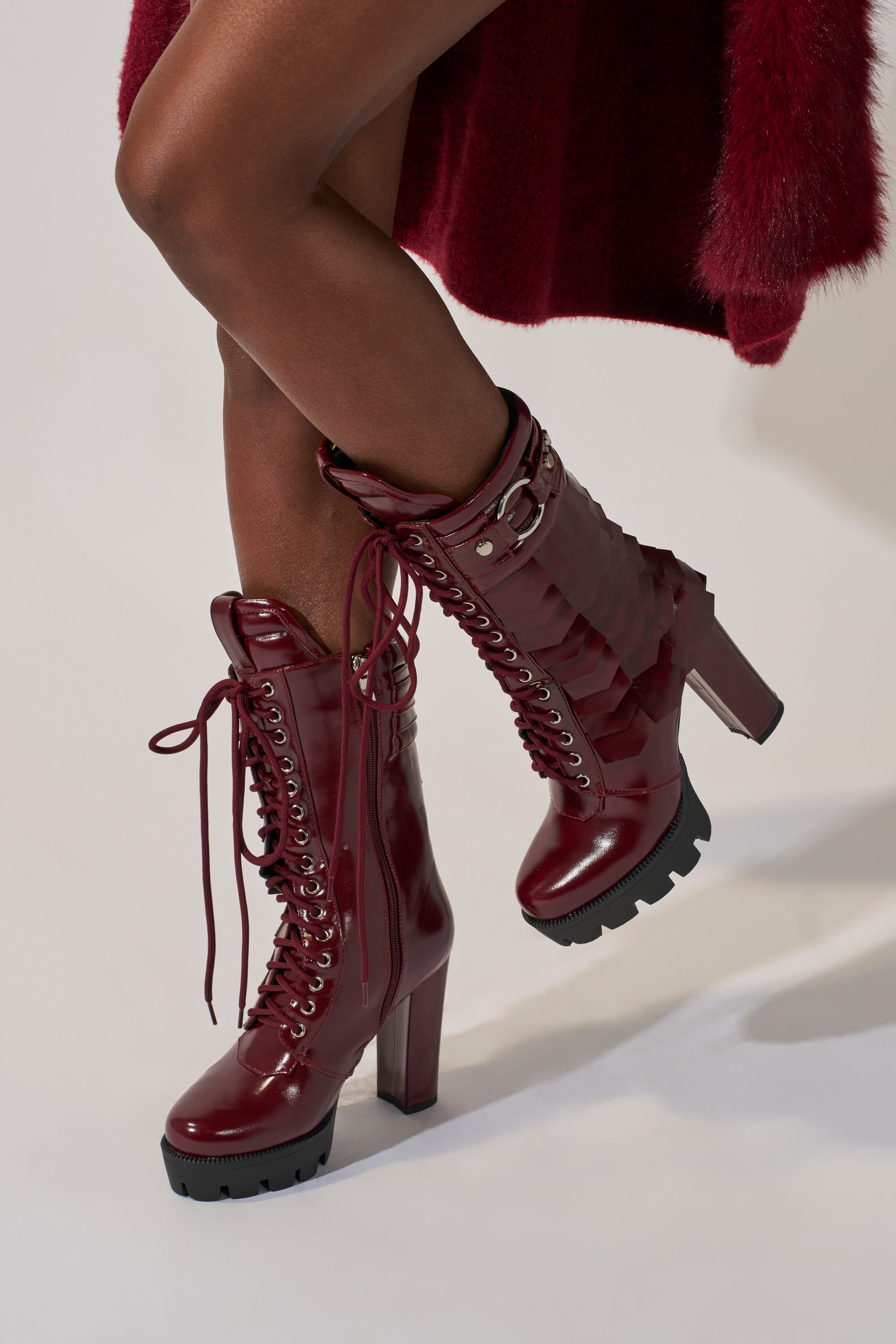 Wearing the AZALEA WANG GERNOT BURGUNDY LACE UP SCALED PLATFORM BOOTIE and a matching burgundy outfit, a person stands against a light background with one leg crossed over the other. 1