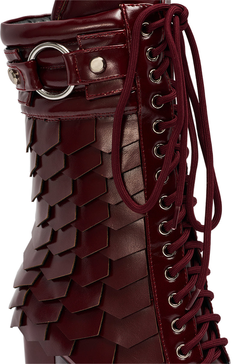 The AZALEA WANG GERNOT BURGUNDY LACE UP SCALED PLATFORM BOOTIE features shiny, burgundy faux leather with layered, scale-like panels, silver eyelets, and matching red laces on the side. 6