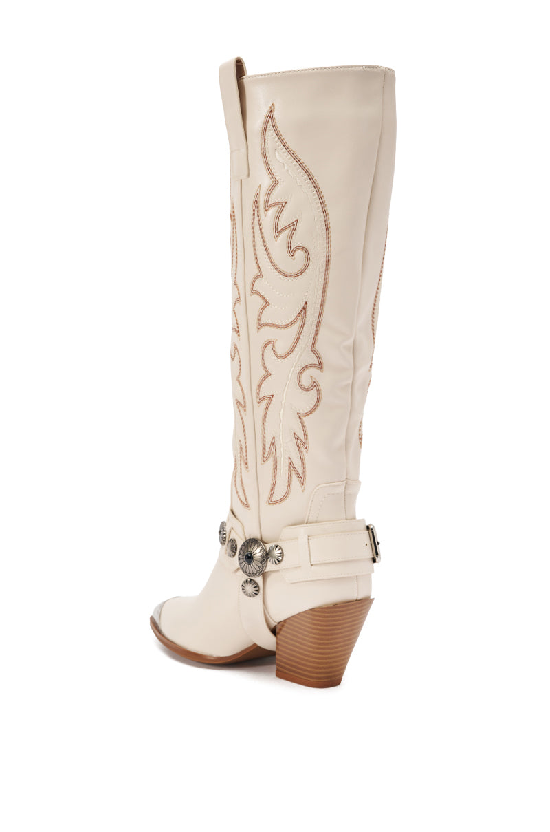 The AZALEA WANG GERVASE BONE PU SILVER HARDWARE WESTERN BOOT is a cream-colored, knee-high faux leather boot with tan stitching, pointed toe, decorative harness with silver conchos, and a stacked brown heel. Displayed on a white background. 6