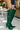 Outdoors, someone adjusts the AZALEA WANG GESINE GREEN CROC PATENT LUXE BOOT—tall, croc-embossed thigh-highs with pointed toes and stiletto heels—paired with a denim skirt or jacket against an urban backdrop.