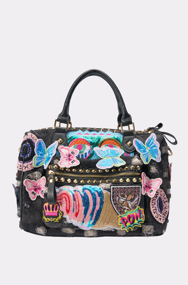Introducing the EYE SEE YOU PATCH DENIM BAG—a distressed black denim handbag adorned with vibrant embroidered patches, featuring butterflies, eyes, rainbows, a tiger, a crown, and the playful word "POW!" Gold studs and worn-in fabric details enhance its edgy streetwear charm.