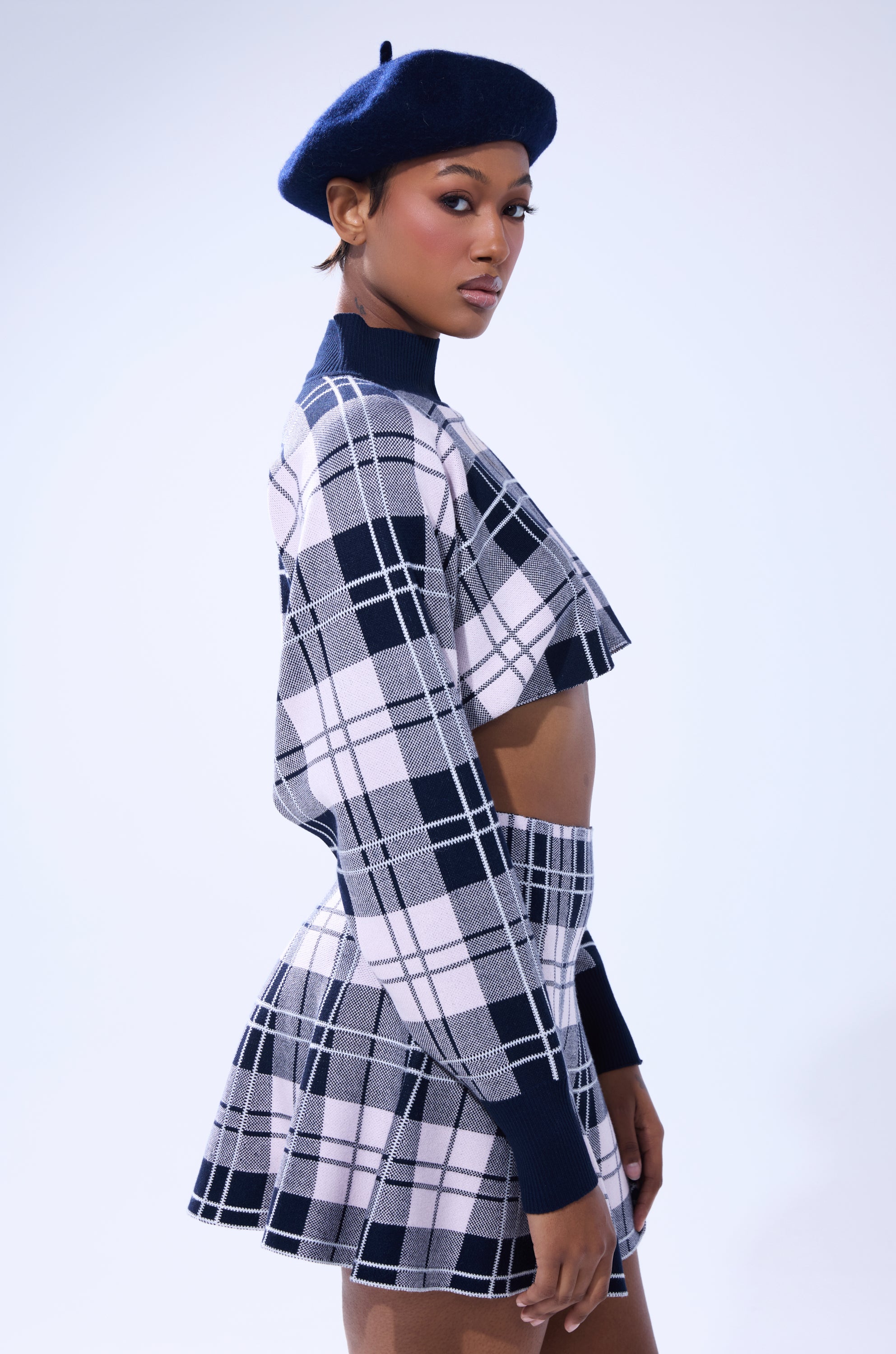 A woman stands in profile against a white background, confidently wearing the HOME FOR THE HOLIDAYS CROPPED SWEATER with a matching skirt and a navy beret. 3