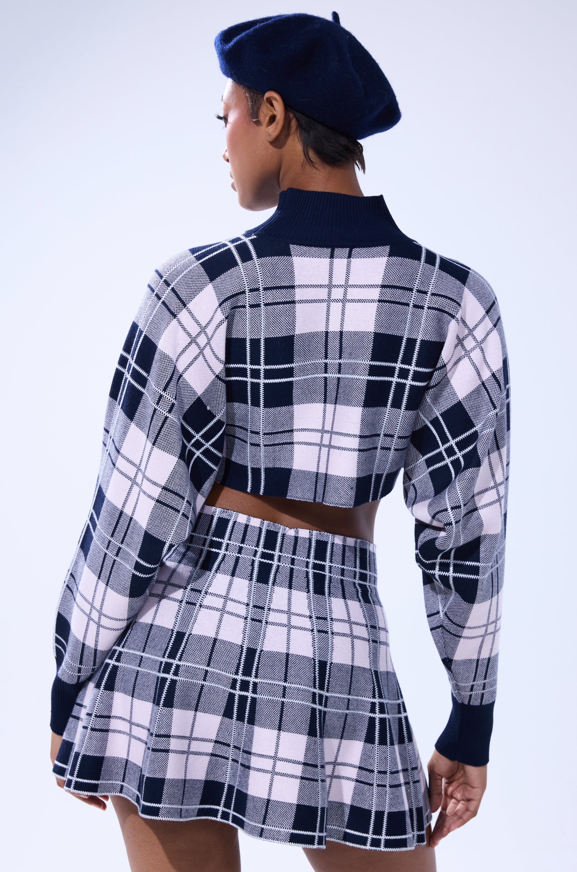 A person wearing a HOME FOR THE HOLIDAYS CROPPED SWEATER with a matching plaid high-waisted skirt and navy beret stands with their back to the camera against a light background. 4