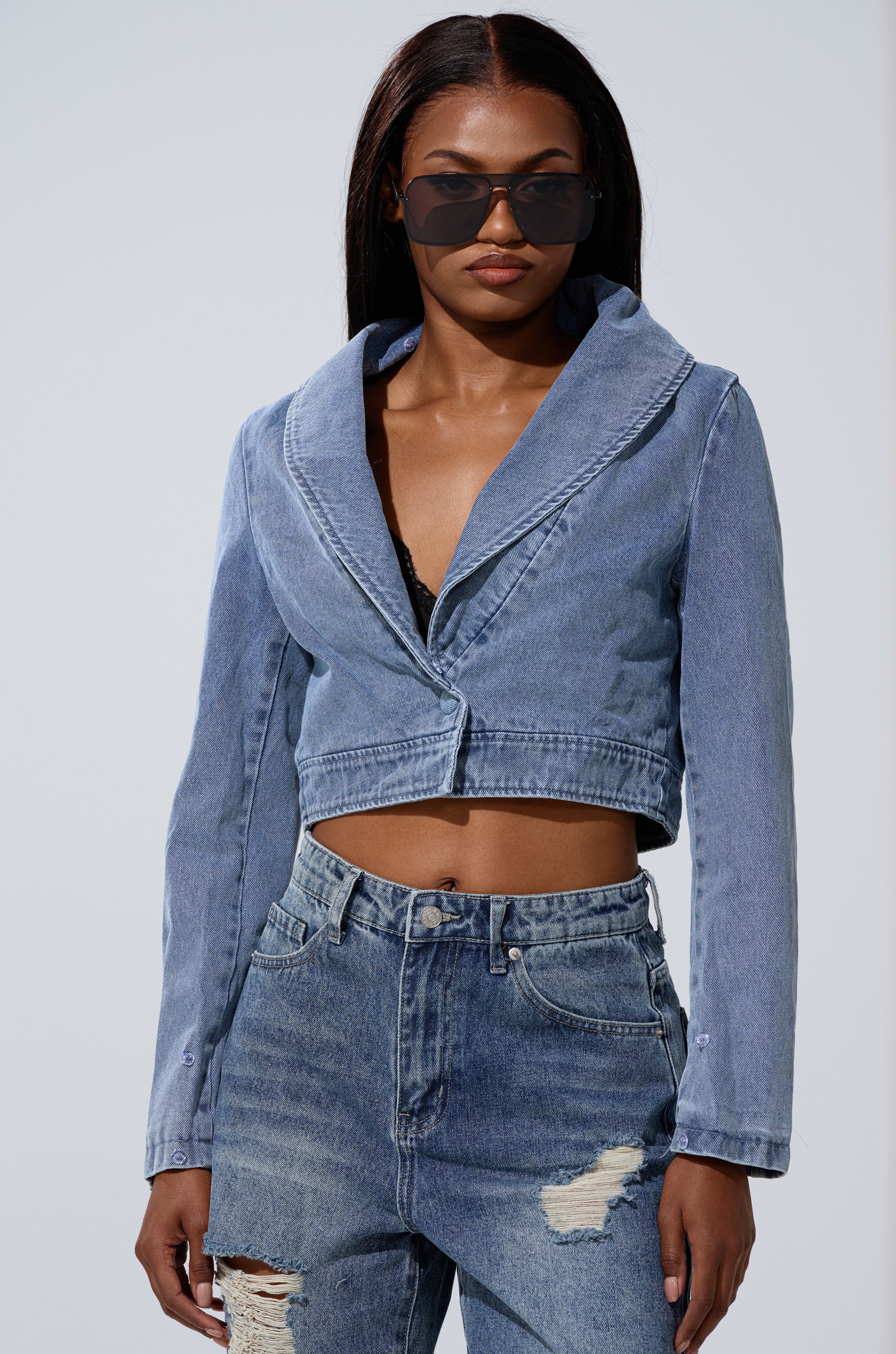 A woman in dark sunglasses, a NEW GISELE CROPPED FUR TRIM JACKET over a black top, and high-waisted distressed jeans stands against a plain light background.
