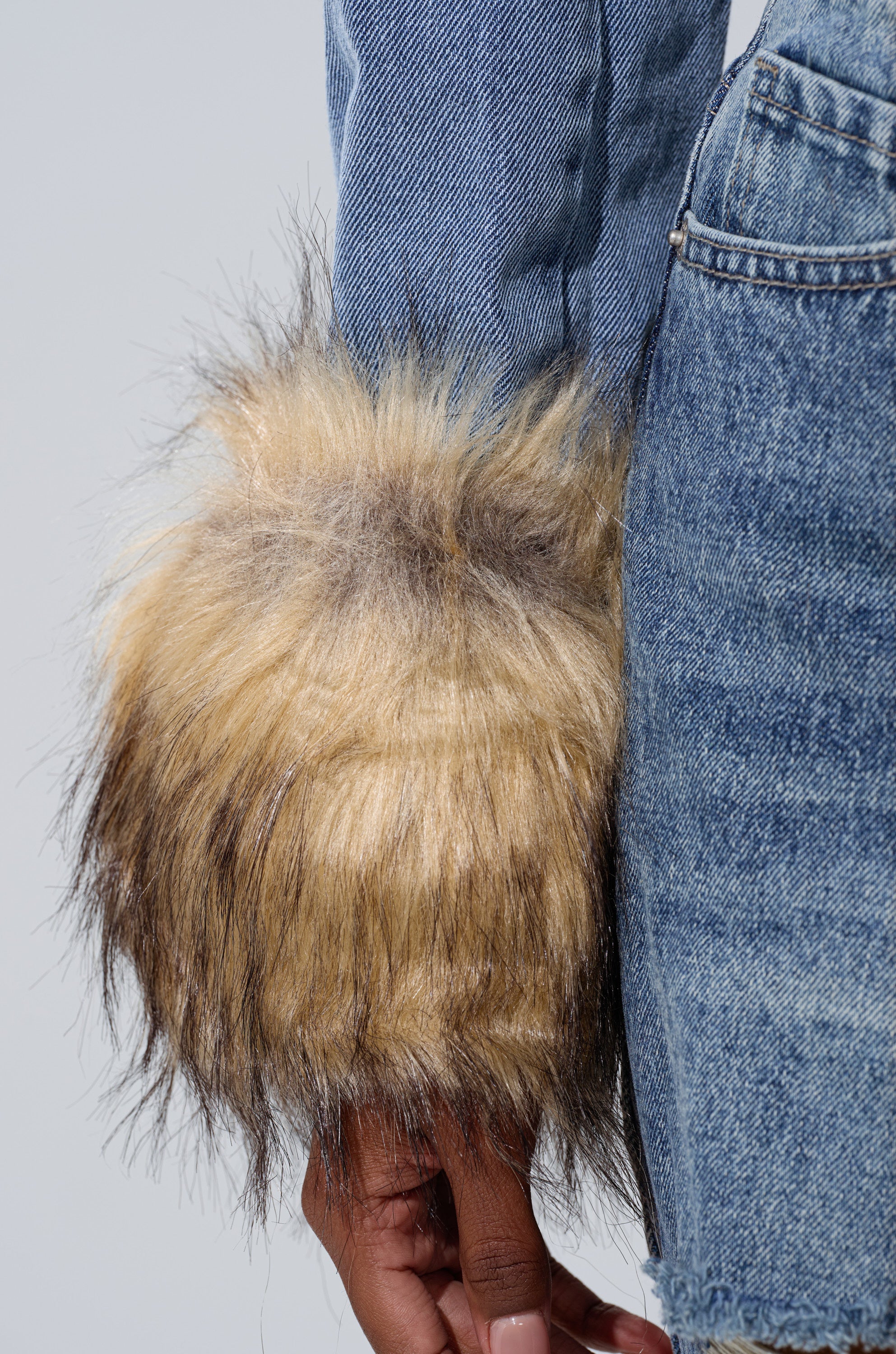 A person wears the NEW GISELE CROPPED FUR TRIM JACKET—blue with thick, light brown fur cuffs—paired with matching denim jeans. The furry sleeves contrast stylishly with the jacket’s smooth blue denim.
