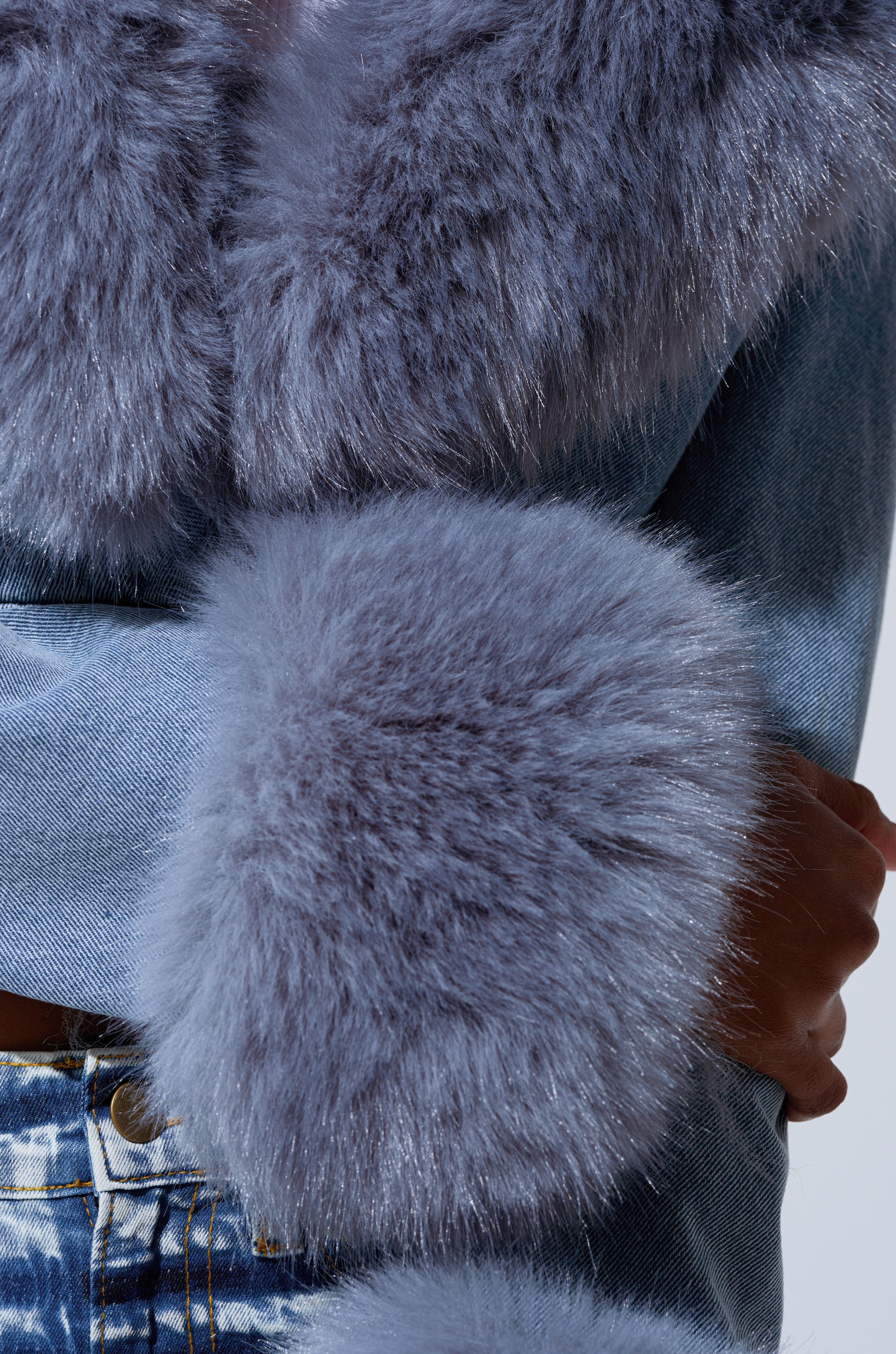 A person in the GISELE CROP DENIM BLAZER featuring Y2K Bratz Doll style, with large, fluffy light purple faux fur trim on the cuffs and collar, shown from the chest down with arms crossed.