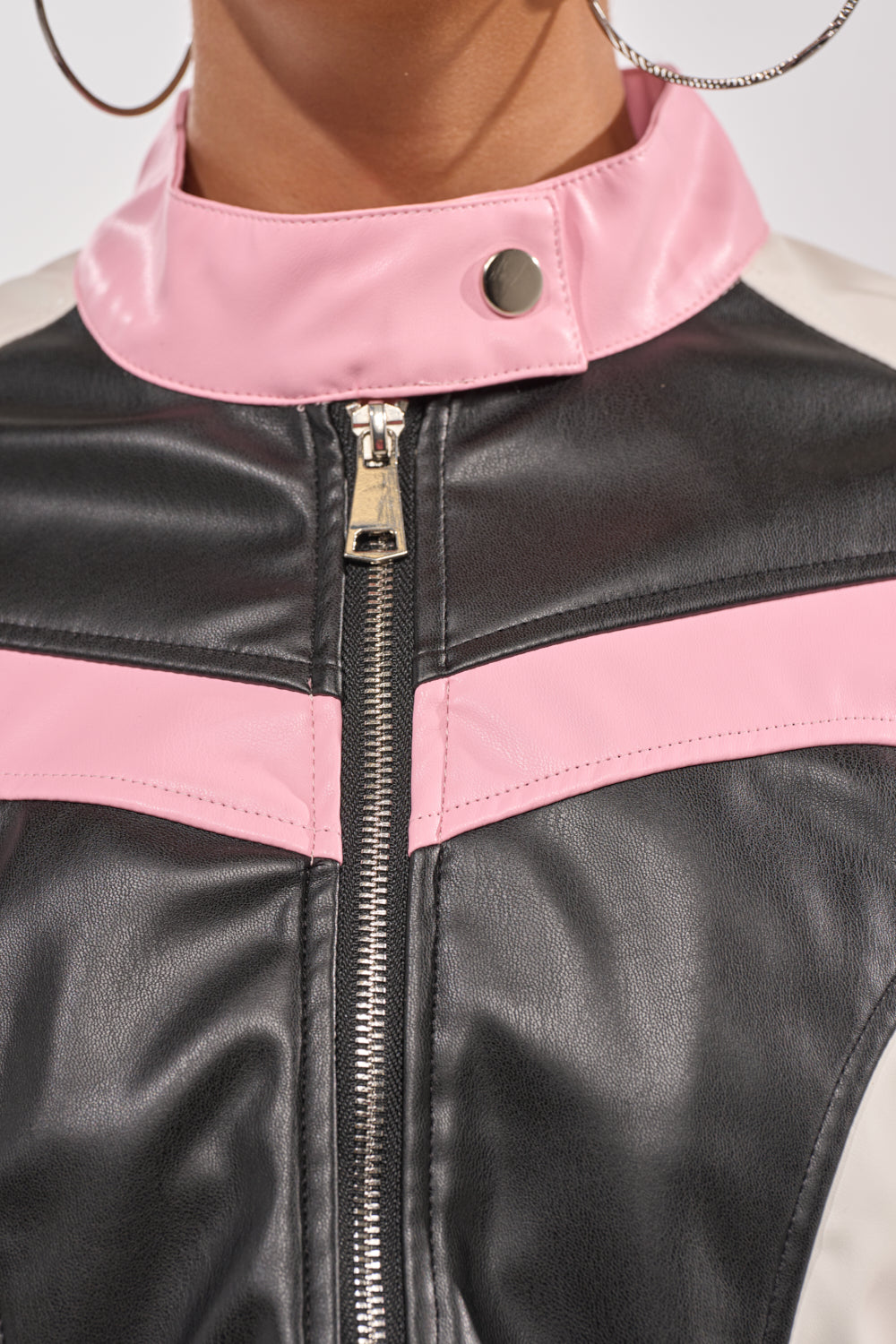Close-up of a person wearing the LILOU EVERYDAY MOTO, a black and pink faux leather jacket with front zipper and silver snap button collar, styled with large silver hoop earrings for a streetwear look. 7