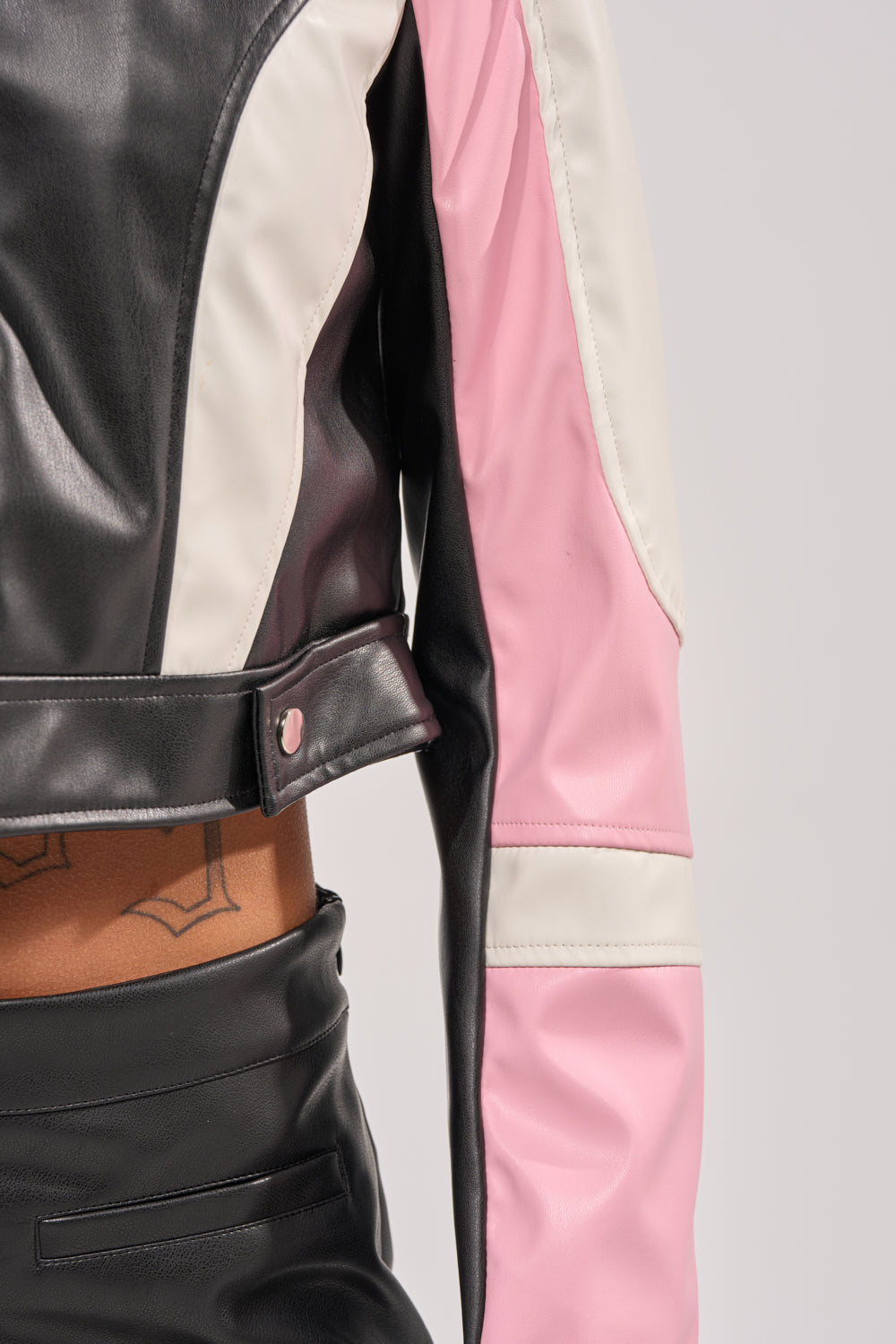 A close-up of a person wearing the LILOU EVERYDAY MOTO jacket and matching pants, revealing their midriff and a geometric lower back tattoo against a plain light background. 8