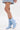 A person in a short, light denim skirt and AZALEA WANG GLACIELLE BLUE WEDGE BOOTIE with a pointed-toe stands against a plain white background.