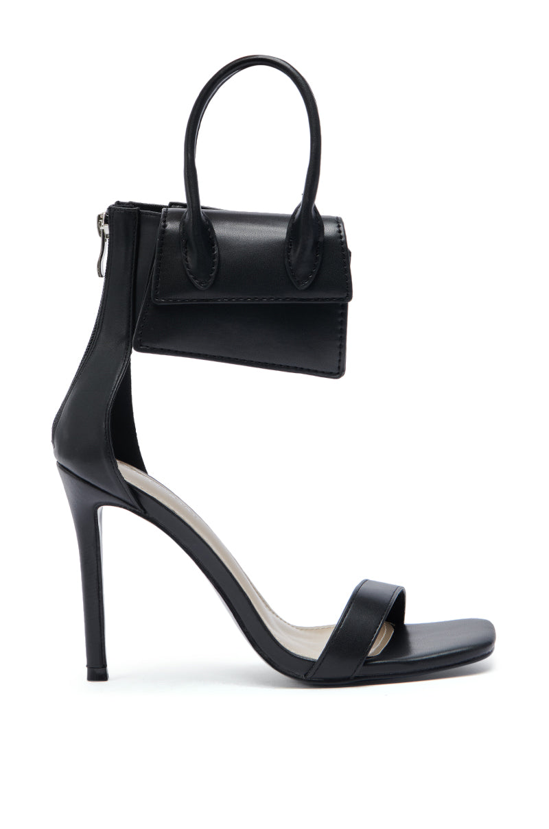 The AZALEA WANG GLENDA BLACK BAG EMBELLISHMENT SANDAL is a black faux leather stiletto with an ankle strap and a unique attached mini handbag, blending footwear and accessory in one standout design. 4