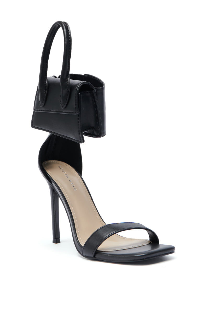 The AZALEA WANG GLENDA BLACK BAG EMBELLISHMENT SANDAL features a black stiletto heel, thin ankle strap, bag embellishment above the heel, minimalist faux leather upper, and beige insole for effortless style. 5