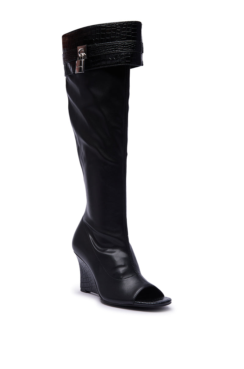 The AZALEA WANG GLENNA BLACK STRETCH PU WEDGE BOOT features black faux leather, a knee-high open toe design, a textured crocodile pattern on the cuff and wedge heel, plus a silver buckle, shown against a white background.
