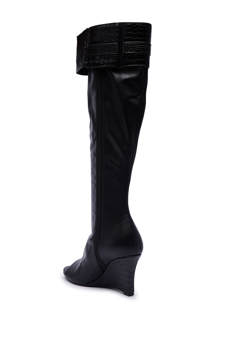 The AZALEA WANG GLENNA BLACK STRETCH PU WEDGE BOOT features a pointed toe, wide cuff, and textured crocodile-pattern details on the cuff and wedge heel. This chic faux leather knee-high boot offers both style and comfort.