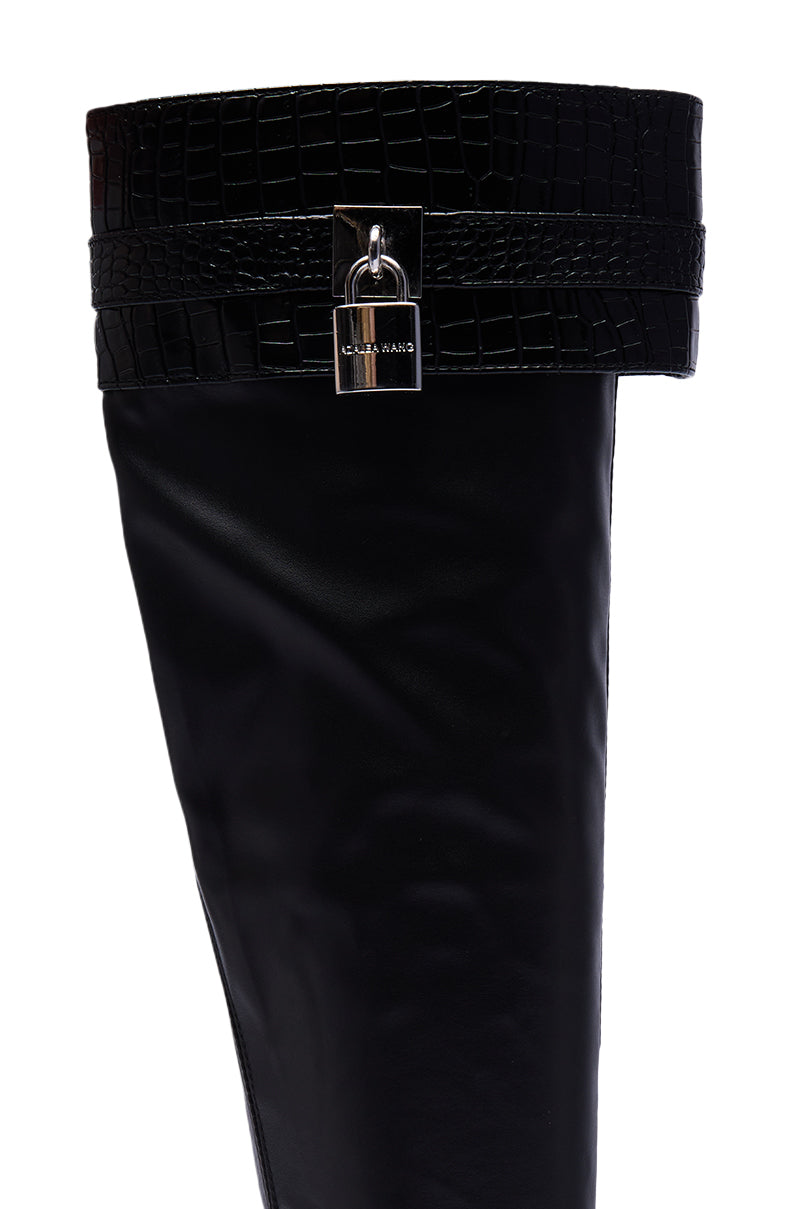 A close-up of the AZALEA WANG GLENNA BLACK STRETCH PU WEDGE BOOT, a black faux leather knee-high with a crocodile-patterned cuff and a silver "MATTE WANG" padlock detail.