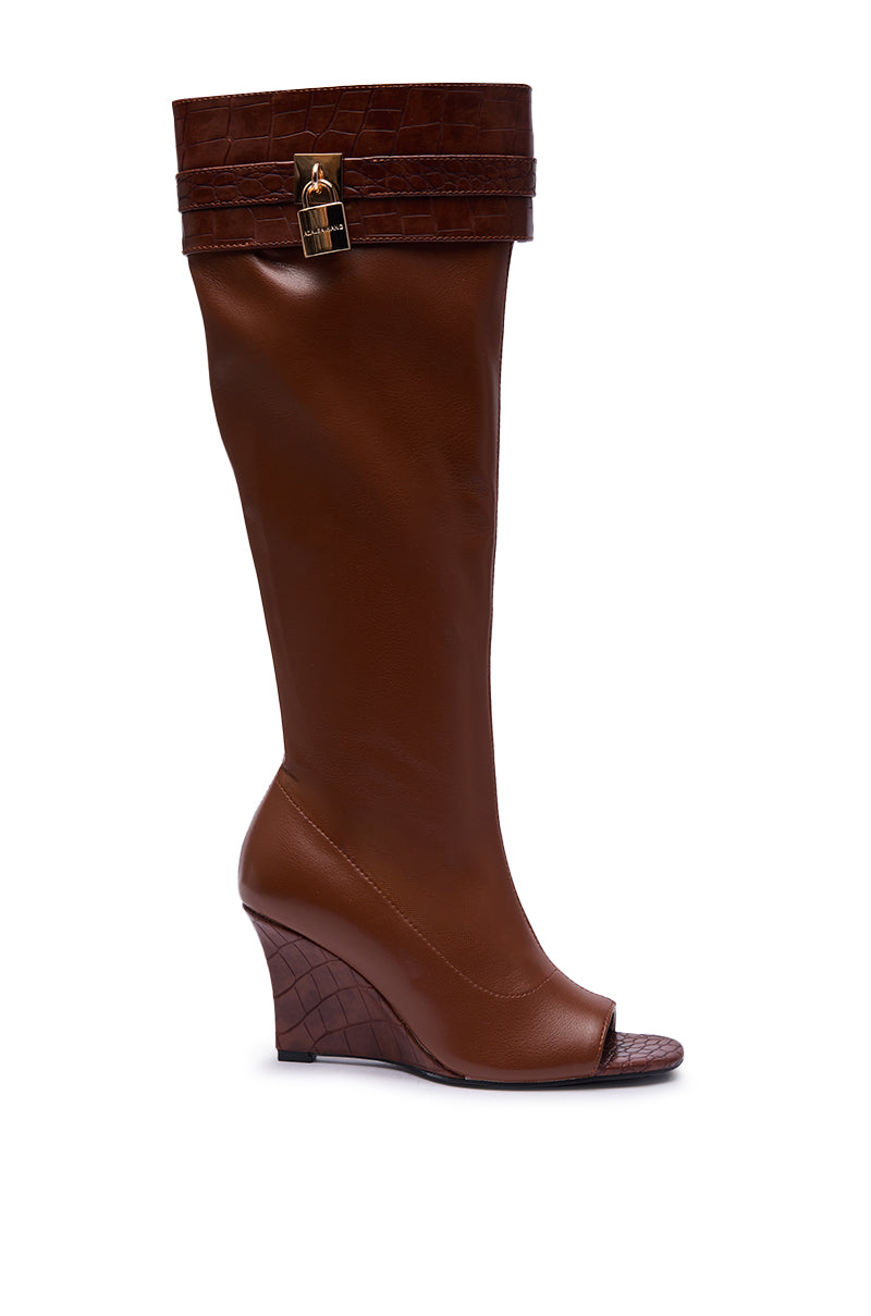 The AZALEA WANG GLENNA COGNAC STRETCH PU WEDGE BOOT is a brown, knee-high faux leather wedge boot featuring crocodile-textured accents at the top and heel, an open toe, and a gold buckle detail near the cuff.