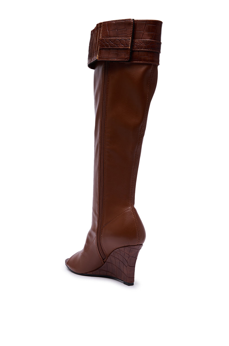 The AZALEA WANG GLENNA COGNAC STRETCH PU WEDGE BOOT is a knee-high, pointed-toe cognac boot with a folded cuff and crocodile-style details on the cuff and wedge heel, displayed against a white background.