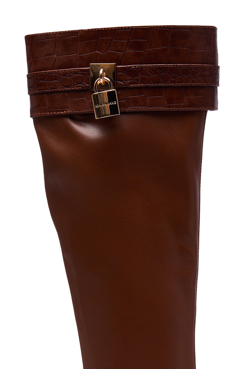 Close-up of the AZALEA WANG GLENNA COGNAC STRETCH PU WEDGE BOOT featuring brown faux leather, a crocodile-patterned cuff, and a gold-colored lock detail on a strap near the top.